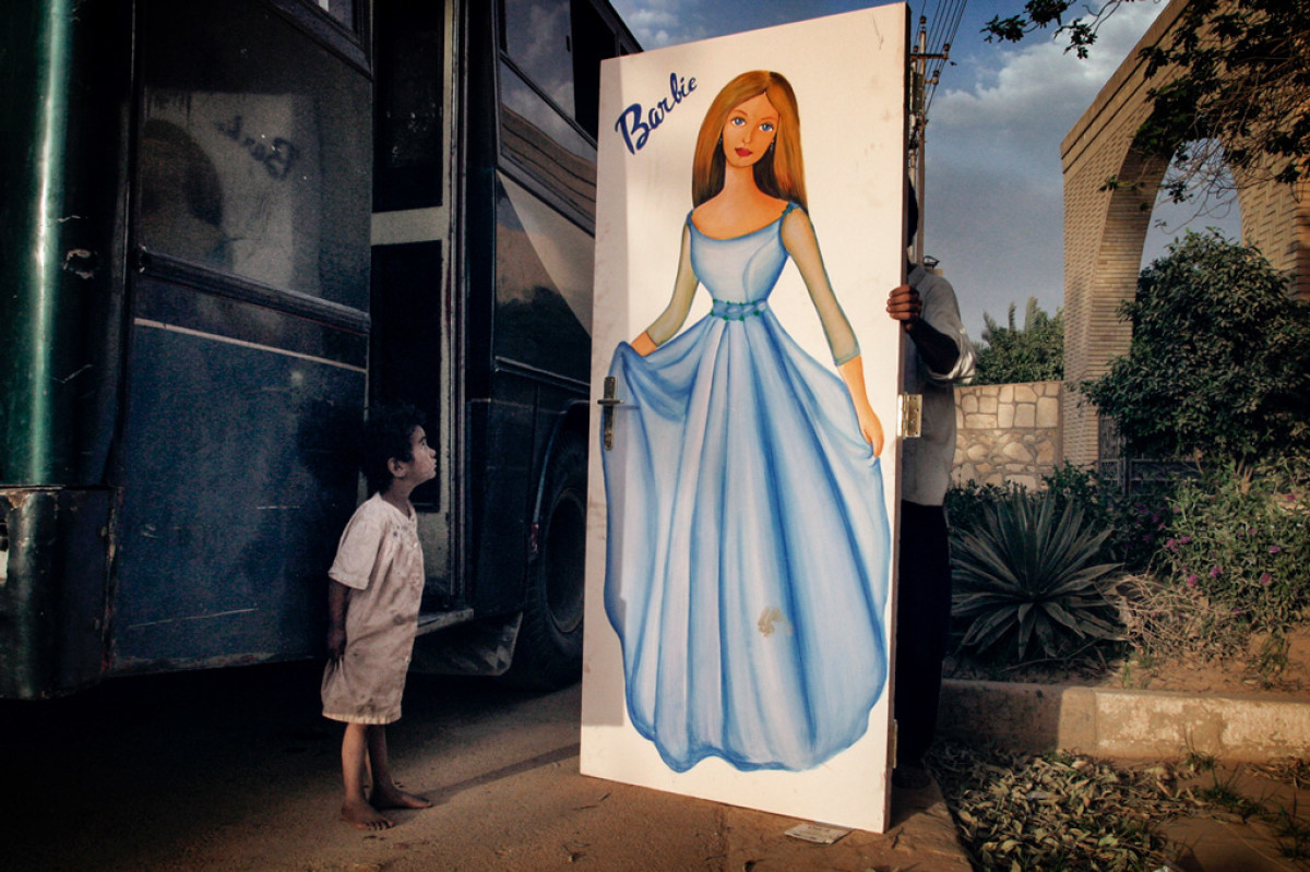 Мальчик смотрит с изумлением на изображение куклы Барби на двери шкафа, которую его отец принес с виллы брата Саддама Хуссейна Ватбана аль-Хасана.